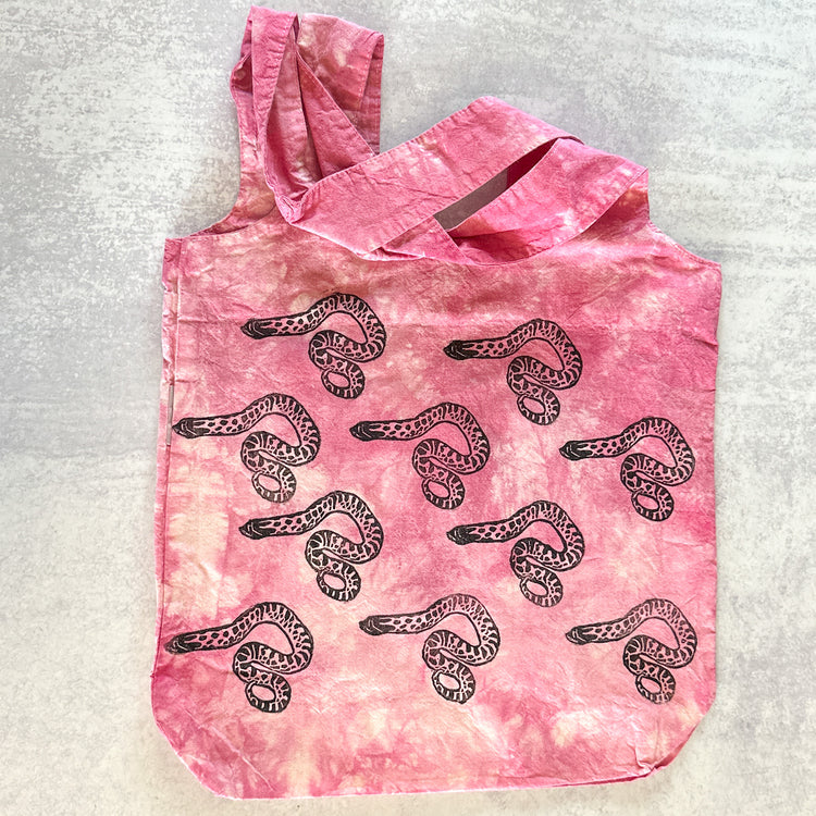 A pink tie-dye tote bag with a repeating pattern of hognose snakes in black ink